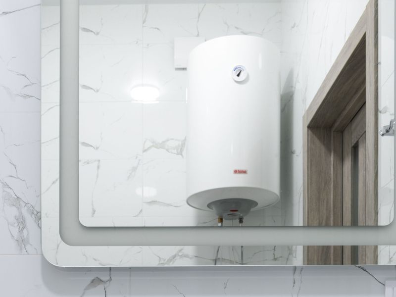 Chauffe-eau électrique mural, vu dans le miroir d'une salle de bain au carrelage effet marbre