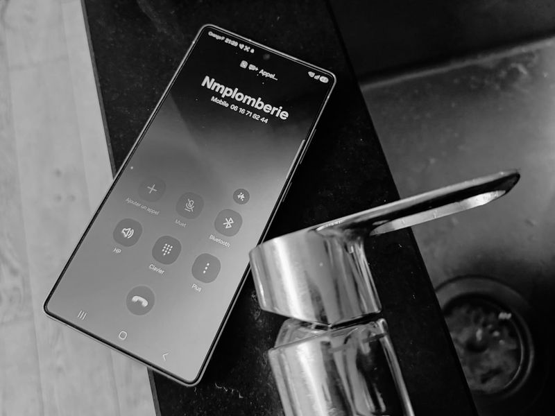 Téléphone affichant un appel en cours vers NM Plomberie, posé au bord d'un lavabo sur un chantier