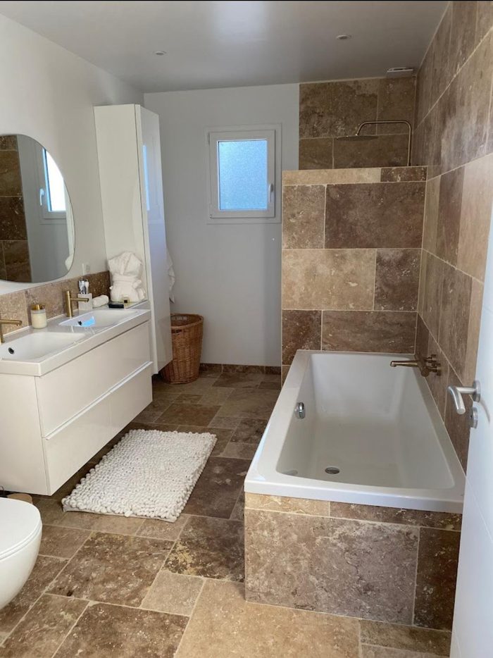 Baignoire habillée de travertin et douche ouverte en robinetterie laiton